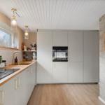 Modern kitchen with wooden surfaces and built-in oven. Shelf with mugs on brick wall.