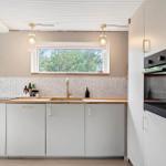 Modern kitchen with worktop, sink and window. White cabinets and backsplash with mosaic.