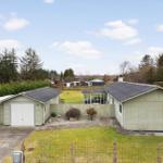 A light green house with a garage and garden. Trees and other houses are visible in the background.
