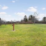 Large green lawn with trees and a red post in the foreground.