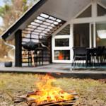A burning fire pit in front of a modern house with a terrace and seating area.