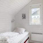 Bedroom with bed, window, and heater against white wood wall.