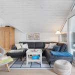 Living room with gray sofa, white table, and wooden wall. Terrace accessible via glass door.