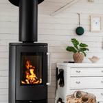 Black wood-burning stove with fire in a room with white wood paneling.