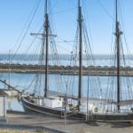 Segelschiffe liegen im Hafen, dahinter sind Solaranlagen und Meer sichtbar.