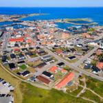 Aerielansicht von Küstenstadt mit Häusern, Hafen und blauem Meer.