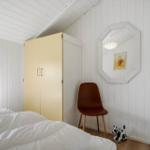 Schlafzimmer mit Bett, Kleiderschrank, Stuhl und Spiegel an der Wand.