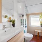 Badezimmer mit Waschbecken, Toilette und Dusche. Holzmöbel, Pflanzen und Fenster.