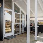 Terrasse mit Tisch und Stühlen unter Dach. Durchgehende Glasfront zur Küche.