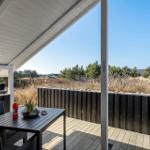 Terrasse mit Tisch, Stühlen und Grill. Blick auf Grasland und Bäume.