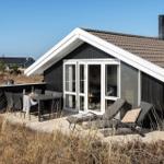 Schwarzes Haus mit Terrasse, Liegen und Grillplatz. Blick auf Strand und Meer.