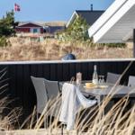 Terrasse mit Tisch und Stühlen, Blick auf Strand und Häuser.