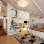 Wohnbereich mit Sofa, Regal und Schlafplatz unter Holzdecke.