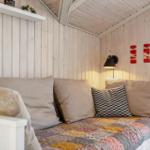 Ein Sofa mit Kissen und Decke in einem holzverkleideten Raum mit Wandlampe und Fenster.