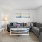 Wohnzimmer mit grauem Sofa, weißem Couchtisch und Wandbild.