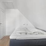 Schlafzimmer mit Dachschräge, Bett, Kleiderschrank und Tür.