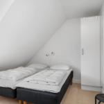 Zimmer mit Doppelbett unter Dachschrägen, weißer Schrank und Wandbild.