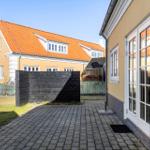 Hinterhof mit Pflasterweg, gelbem Haus und rotem Dach. Schwarze Holzwand und Fenster sichtbar.