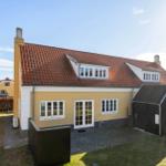Gelbes Haus mit rotem Dach, weißen Fenstern und kleinem Schuppen.