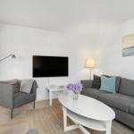 Wohnzimmer mit grauem Sofa, weißem Couchtisch und Fernseher an der Wand.