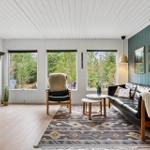 Living room with sofa, armchair, and windows to nature.