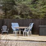 Deck with table, chairs, and wooden flooring in front of dark fence and forest.
