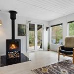 Living room with fireplace, TV, and seating. Large windows offer view of outdoor area.
