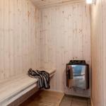 Sauna with wooden walls and bench, beside heater with stones.