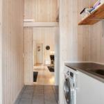 Hallway with washing machine and wooden wall, view into living area with chair and clock