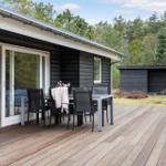 Deck with table and chairs in front of a house with wood siding and sliding doors.