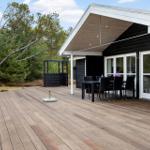 Wooden terrace with table and chairs in front of modern house with large windows.