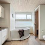 Bathroom with bathtub, toilet, and sauna. Wooden ceiling and window with view.