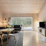 Living room with wood walls, sofa, fireplace, and TV. View of forest through glass door.