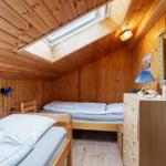 Room with two beds, wooden walls, and skylight. Dresser with mirror and lamp.