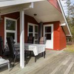 Red wooden house with deck, table, chairs, and lounge chair outside.
