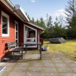 Red wooden house with patio, table, bench, and garden. Forest and large stone in background.
