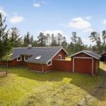 Red wooden house with garage and forest in the background.