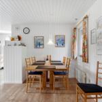 Dining room with wooden table, chairs, and white walls. Window with colorful curtains.