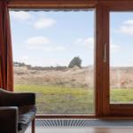 Ein braunes Sofa vor einem großen Fenster mit Blick auf eine Wiese und einen Baum.