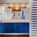 Badezimmer mit blauem Waschbeckenunterschrank und Spiegel. Doppelwaschbecken und Handtuchhalter sichtbar.