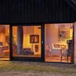 Durch große Fenster ist das Innere mit Kamin, Stühlen und Möbeln sichtbar.