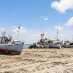 Fischerboote liegen auf Sandstrand, Himmel klar, Traktor zwischen Booten.