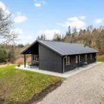 Modern black cabin with terrace, surrounded by forest and grass.
