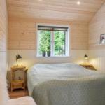 Bedroom with wooden walls, window, and bed with coverlet.