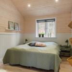 Bedroom with wooden walls, bed, and window with view of forest.