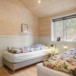 Two beds with floral bedding, wooden walls, and window with view of forest.