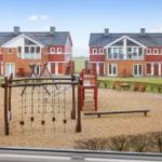 Spielplatz mit Sand und Holzgerüsten vor roten Ferienhäusern.