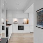 Moderne Küche mit weißen Schränken und Holzboden. Aufgehängte Bilder schmücken die Wände.