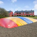 Farbiger Spielplatz vor rotem Ferienhaus mit Grünflächen.