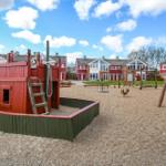 Kinderbereich mit Schiffsspielzeug und Schaukeln vor Wohnhäusern.